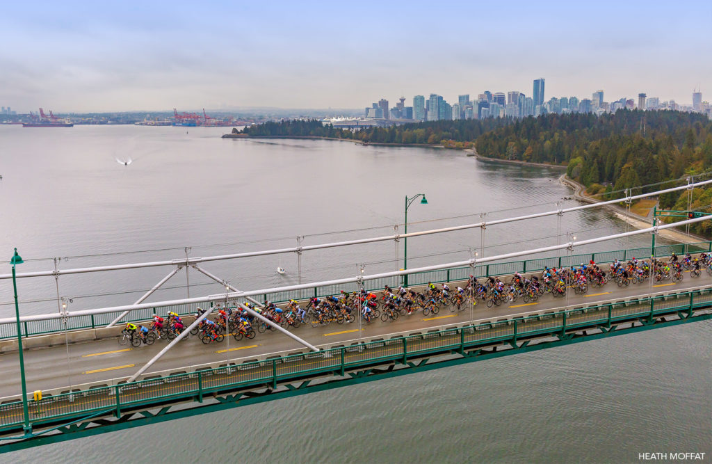 A large group of cyclists cross the Lions Gate bridge with Vancouver and Stanley Park in the background