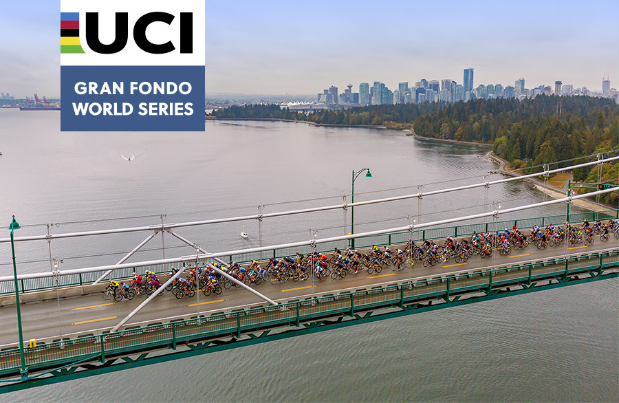 A large group of cyclists cross the Lions Gate bridge with Vancouver and Stanley Park in the background with UCI Gran Fondo World Series logo